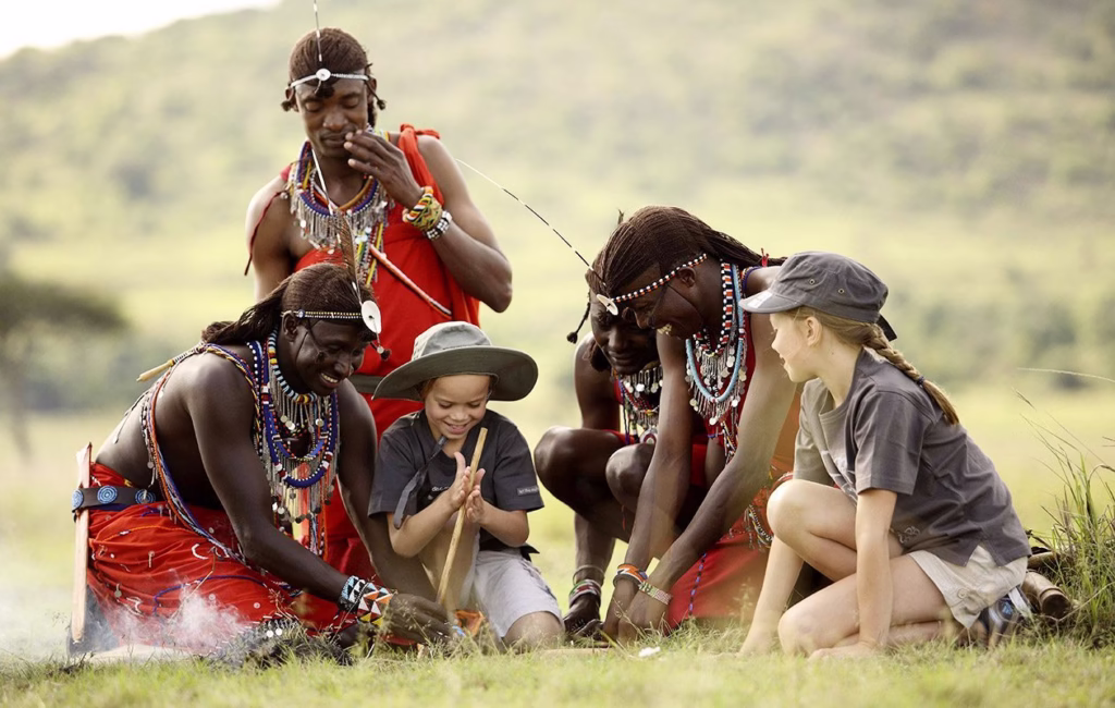 Smiling Maasai men teaching children how to make fire with sticks during a cultural visit in Tanzania