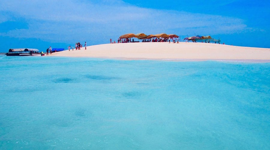 Tourists relaxing under umbrellas on Nakupenda Sandbank surrounded by turquoise sea